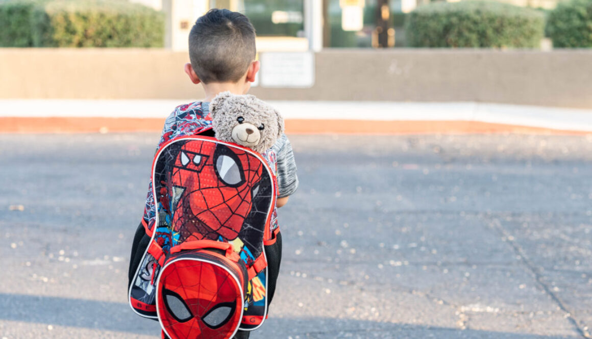 Photograph of an excited 5-year-old boy with backpack and favorite toy, eagerly looking out at his new school