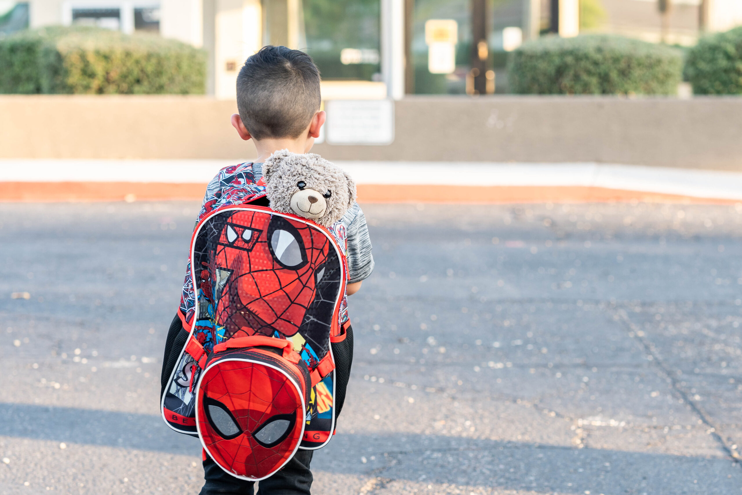 Photograph of an excited 5-year-old boy with backpack and favorite toy, eagerly looking out at his new school