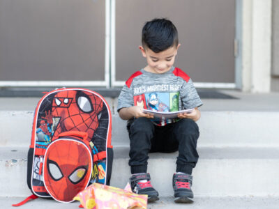 Inquisitive young student, backpack filled with a gift, eagerly anticipates his first day of school