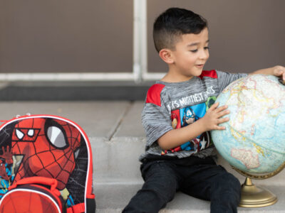 Photo of a 5-year-old boy, looking at a globe, excitedly awaits the start of school