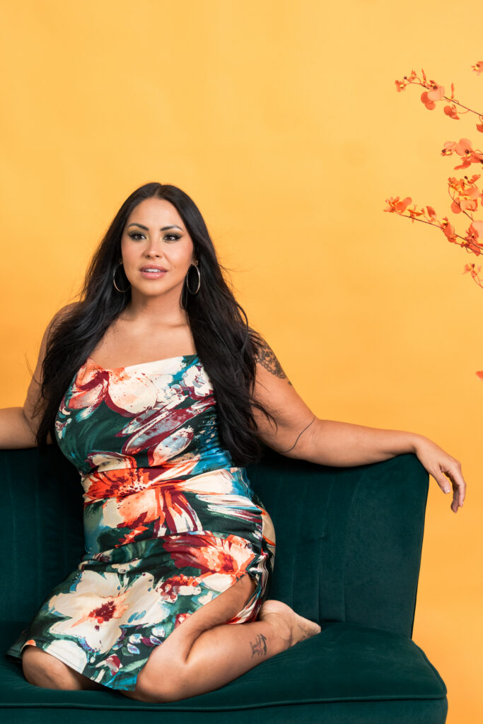 TC wearing an emerald green and coral tropical dress while sitting on a green couch in a colorful studio setting.